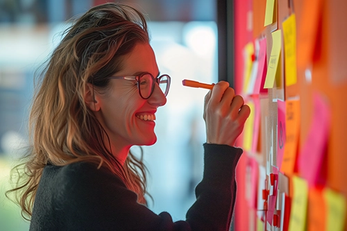 A woman, an innovation strategist with glasses, is looking at sticky notes on a wall.