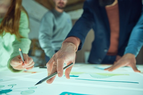 A group of people pointing at a drawing on a table. They are going through the importance of having an innovation strategy.